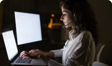 A CakePHP developer woman wearing a headset and typing on a laptop, showcasing Dinoustech's dedication to transparency with expert.